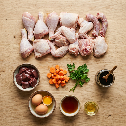 Raw chicken parts, beef liver in a bowl, vegetables, eggs and sauces on a wooden surface