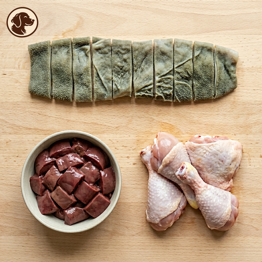 Sliced green tripe, raw chicken pieces, and a bowl of chopped beef liver on a wooden surface, with a dog silhouette icon in the top-left corner.