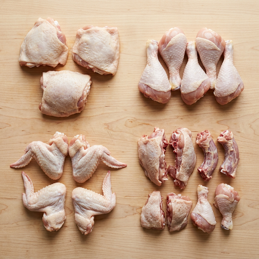 Raw chicken parts including thighs, drumsticks, wings, and breasts on a wooden surface.
