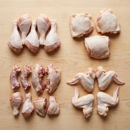 Raw chicken parts including legs, thighs, and wings on a wooden surface.