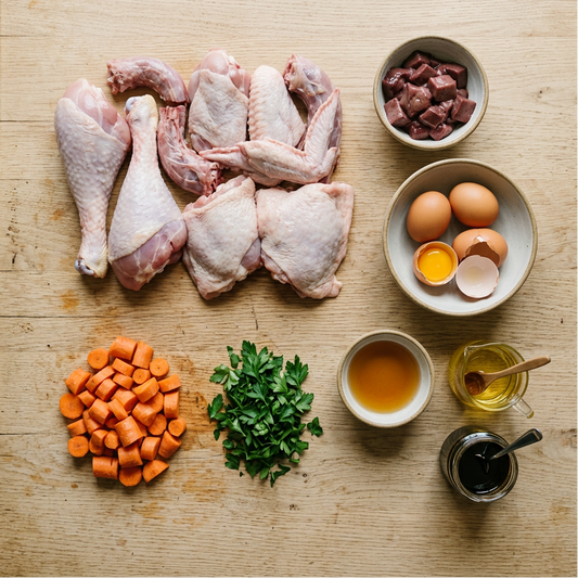 Raw turkey pieces, bowl of beef liver, vegetables, and seasonings on a wooden surface